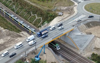 Widok z góry na pociąg jadący po torze pod nowym wiaduktem drogowym w Warce. Po wiadukcie jadą samochody, fot. Artur Lewandowski