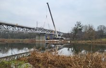 Montaż nowego przęsła mostu na moście kolejowym nad Wartą w Obornikach, na pierwszym planie zarośla i rzeka, w tle drzewa_fot.Radek Śledziński