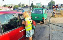 Koordynator wręcza ulotkę kierowcy w samochodzie stojącym przed zamkniętym przejazdem.