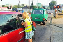 Koordynator wręcza ulotkę kierowcy w samochodzie stojącym przed zamkniętym przejazdem.