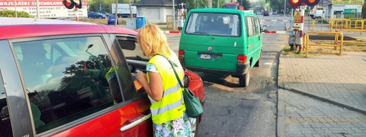 Koordynator wręcza ulotkę kierowcy w samochodzie stojącym przed zamkniętym przejazdem.
