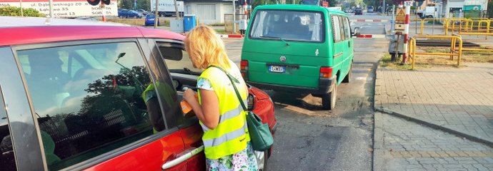 Koordynator wręcza ulotkę kierowcy w samochodzie stojącym przed zamkniętym przejazdem.