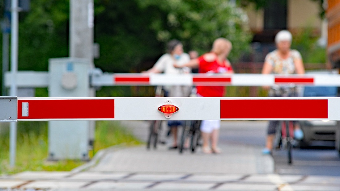 Zbliżenie na zamknięte szlabany. Przed nimi 3 kobiety na rowerach.